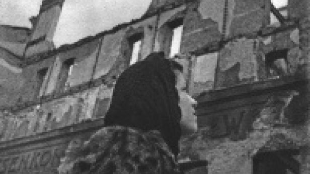Eine Frau steht vor einem zerstörten Gebäude.