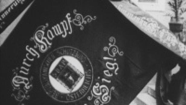 Eine schwarz-weiße Aufnahme einer Fahne mit der Aufschrift „Durch Kampf zum Sieg!“.