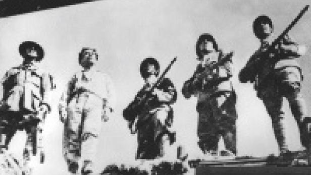 Fünf Soldaten stehen mit Gewehren auf einer erhöhten Plattform.