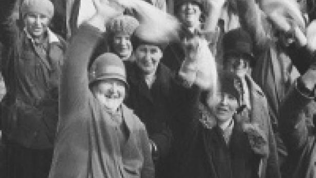 Eine Menschenmenge in Hüten und Mänteln winkt und jubelt.