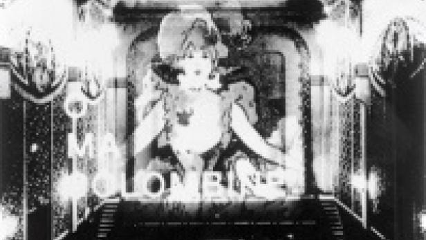 Eine Schwarzweißaufnahme eines alten Kinosaals mit einem Werbeplakat für „Mala Colombé“.