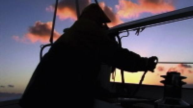 Eine Person steuert ein Segelboot bei Sonnenuntergang.