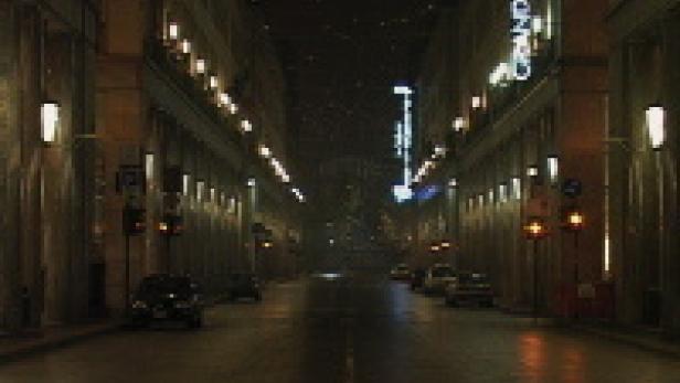 Eine menschenleere Straße in der Nacht mit beleuchteten Gebäuden auf beiden Seiten.