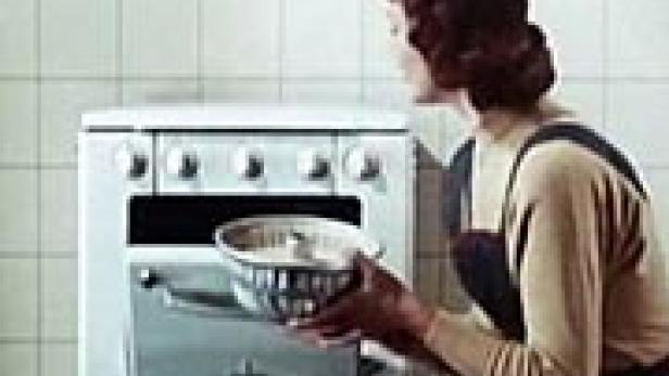 Eine Frau schiebt einen Kuchen in einen Ofen.