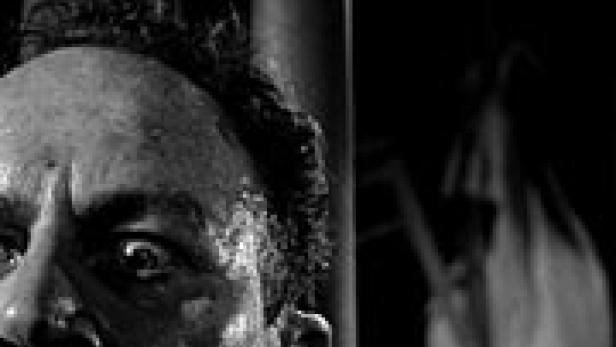 Nahaufnahme eines Mannes mit panischem Gesichtsausdruck, im Hintergrund eine verschwommene, geisterhafte Gestalt.