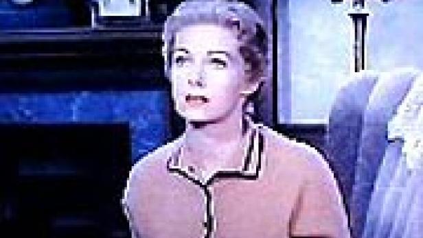 Eine Frau mit blonden Haaren sitzt in einem Sessel und schaut nach oben.