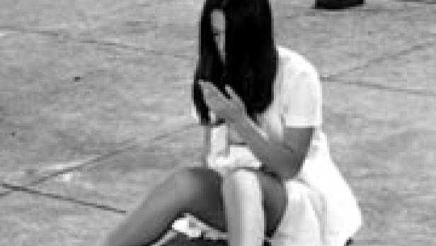 Eine junge Frau sitzt auf dem Boden und schaut auf ihre Hände.