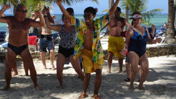 Eine Gruppe von Menschen tanzt am Strand unter Palmen.