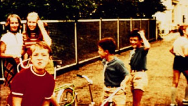 Eine Gruppe Kinder steht und spielt im Freien neben einem Fahrrad.