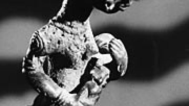 Eine dunkle Skulptur, die eine stilisierte menschliche Figur darstellt.