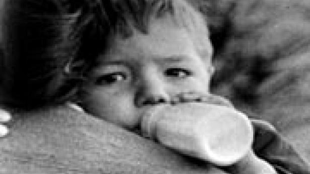 Ein Kind trinkt aus einer Flasche, gehalten von einer Person.