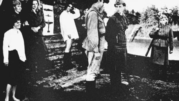 Eine Gruppe von Soldaten und Zivilisten steht im Freien, einige mit Gewehren.