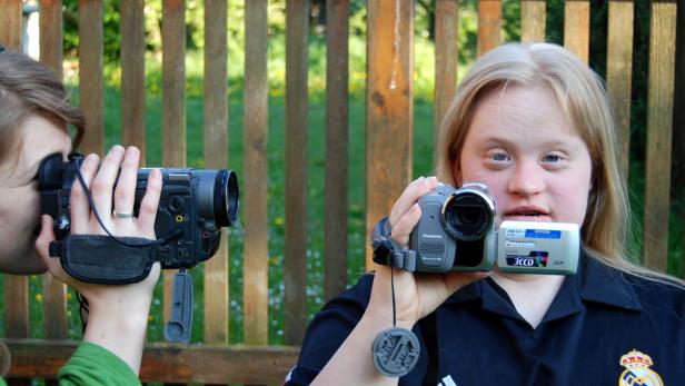 Zwei junge Frauen filmen mit Camcordern vor einem Holzzaun.