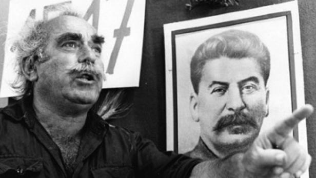 Ein Mann mit Schnurrbart gestikuliert vor einem Porträt von Stalin.