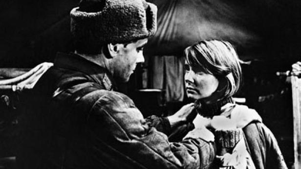 Ein Mann in Uniform und Mütze richtet den Kragen einer jungen Frau.