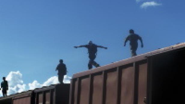 Mehrere Personen balancieren auf dem Dach eines Güterzuges.