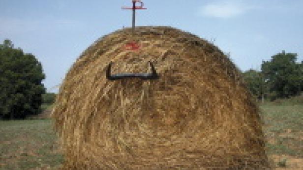 Ein großer Heuballen steht auf einem Feld unter blauem Himmel.