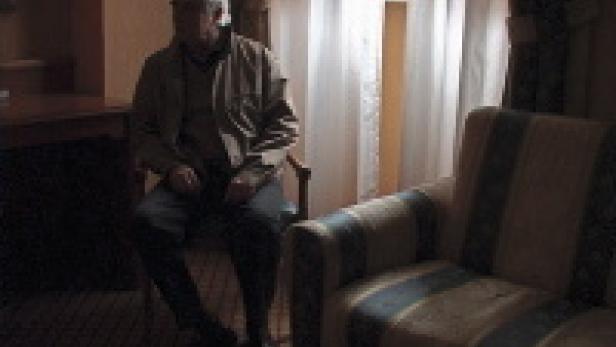 Ein älterer Mann sitzt in einem Zimmer auf einem Stuhl.