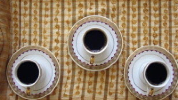 Drei Tassen Kaffee stehen auf einer gemusterten Tischdecke.