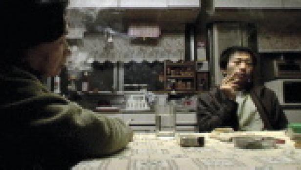 Zwei Männer sitzen an einem Tisch und rauchen Zigaretten.