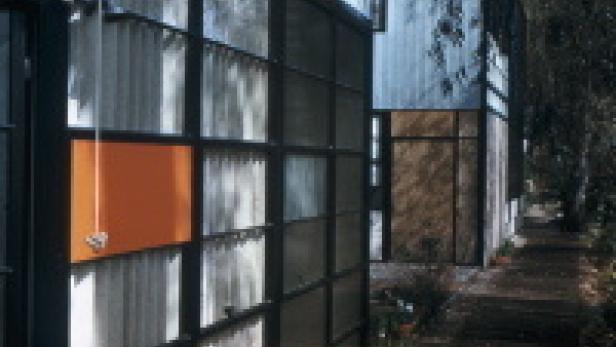 Außenansicht eines modernen Hauses mit großen Fensterflächen und farbigen Paneelen.