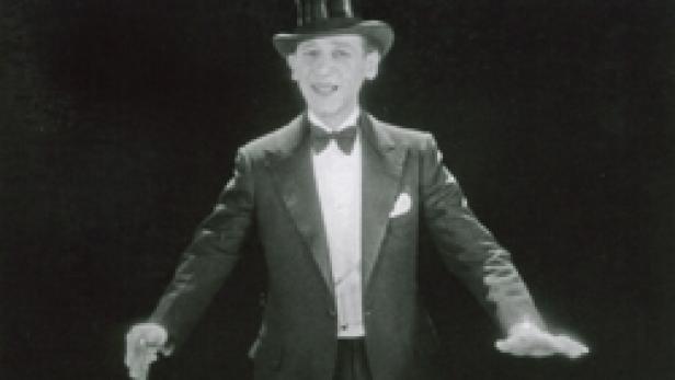 Ein Mann mit Zylinder, Anzug und Fliege singt oder spricht.