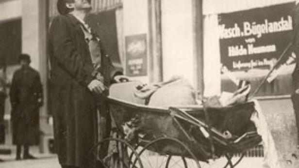 Ein Mann mit Hut schiebt einen Kinderwagen und blickt nach oben.