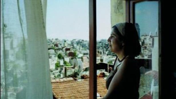 Eine Frau blickt aus einem Fenster auf eine Stadtlandschaft.