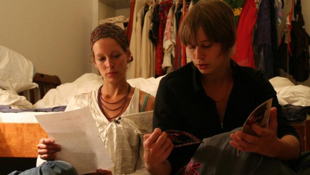 Zwei junge Frauen sitzen auf dem Boden und lesen einen Brief und eine Broschüre.