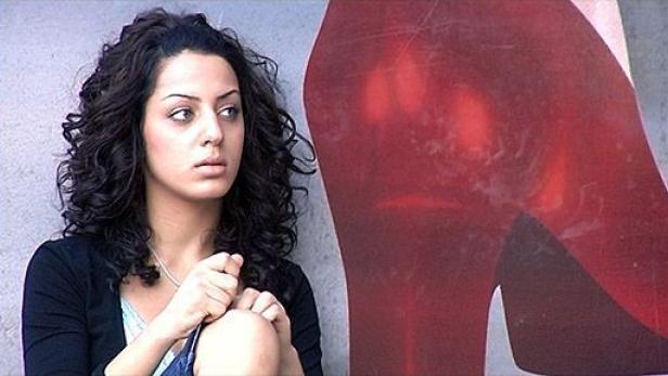 Eine junge Frau mit lockigem Haar sitzt neben einem roten High-Heel-Schuh-Graffiti.