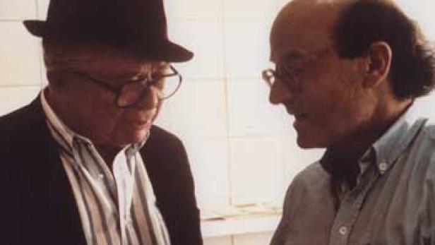 Zwei Männer unterhalten sich, einer trägt einen Hut.