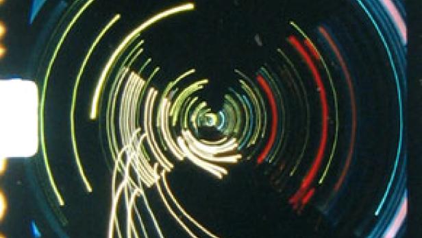 Kreisförmige Lichtspuren in Gelb, Rot und Blau auf schwarzem Hintergrund.