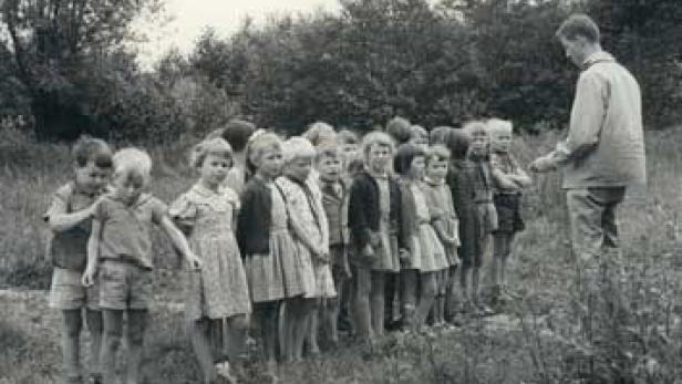 Eine Gruppe Kinder steht mit einem Mann in einer Reihe auf einer Wiese.