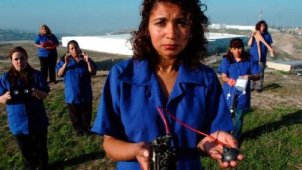Eine Frau hält ein elektronisches Gerät in den Händen, während andere Frauen im Hintergrund stehen.