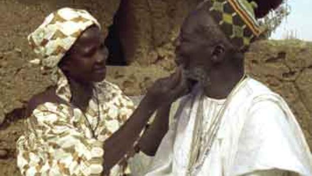 Eine Frau berührt den Bart eines älteren Mannes im Freien.