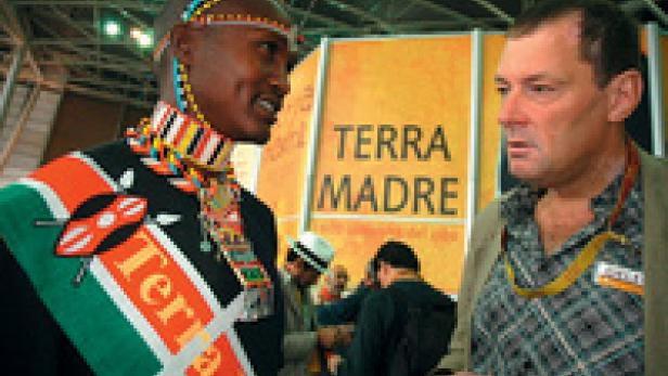 Ein Mann in traditioneller afrikanischer Kleidung spricht mit einem Mann in westlicher Kleidung vor einem „Terra Madre“-Schild.
