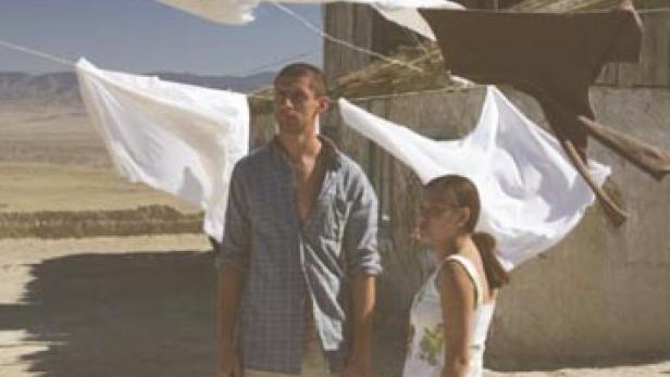 Ein junges Paar steht vor einem Haus, an dem Wäsche zum Trocknen aufgehängt ist.