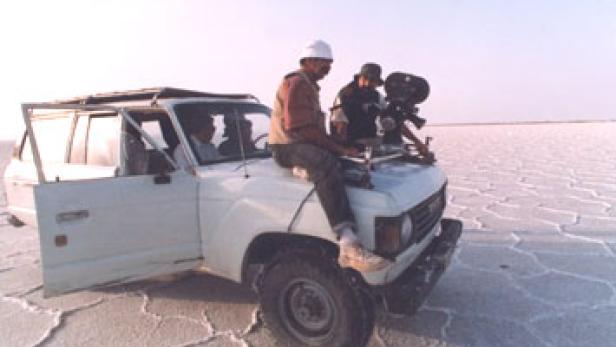 Zwei Männer mit Kamera auf einem Geländewagen in einer weiten, flachen Landschaft.