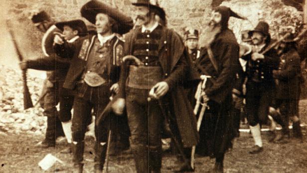 Eine Gruppe von Männern in Trachten steht vor einer Steinmauer.