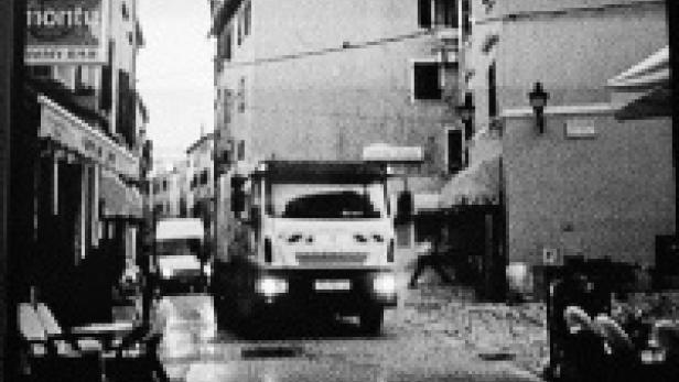 Ein Müllwagen fährt durch eine enge Gasse in einer Stadt.