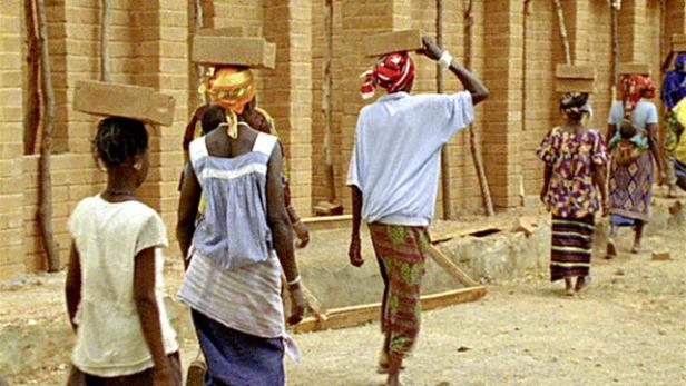 Frauen tragen Ziegelsteine auf ihren Köpfen zu einer Baustelle.