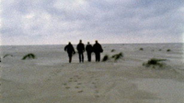 Vier Personen gehen an einem bewölkten Tag am Strand entlang.