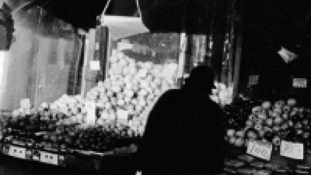 Ein Mann steht vor einem Marktstand mit Obst und Gemüse.