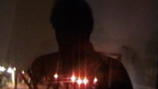 Eine Person steht im Dunkeln vor einer Reihe von Kerzen.