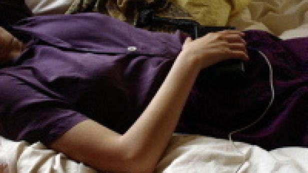 Eine Frau liegt mit einem Smartphone in der Hand auf einem Bett.