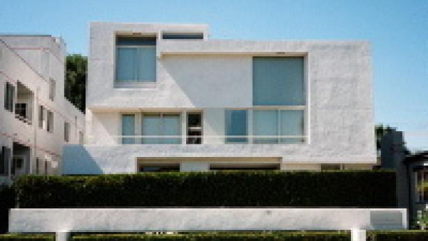 Ein modernes, weißes Haus mit großen Fenstern und einer grünen Hecke im Vordergrund.