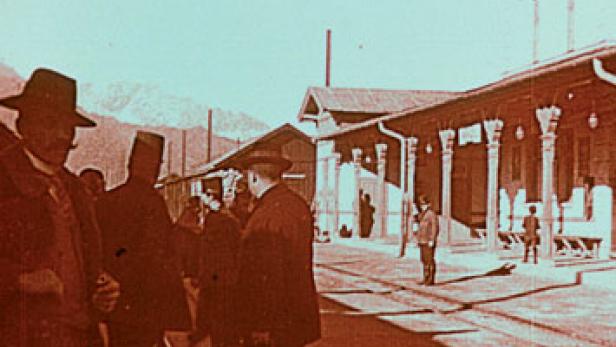 Eine Gruppe von Männern mit Hüten steht vor einem Bahnhofsgebäude.