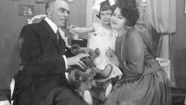 Eine Familie sitzt zusammen und spielt mit einem Teddybären.