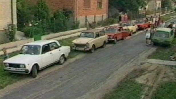 Eine Reihe geparkter Autos säumt eine Straße in einer ländlichen Gegend.