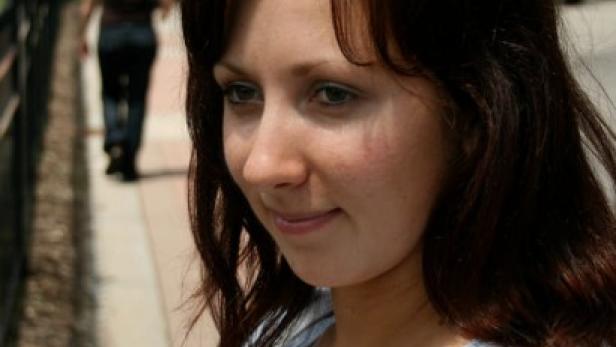 Eine junge Frau mit braunen Haaren lächelt leicht.